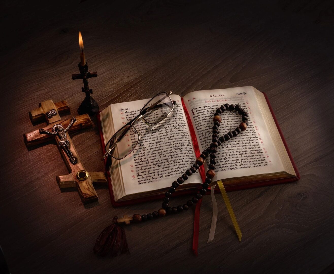 A book, rosary and a candle on a wooden table.